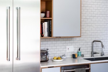 встроенная кухонная раковина и кухонный смеситель с белыми столешницами и шкафами и фартуком из плитки метро